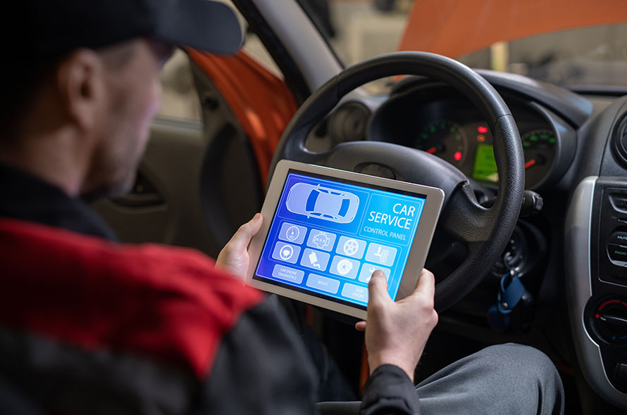 A person inside a car holds a tablet displaying a digital car service control panel with various icons and functions.